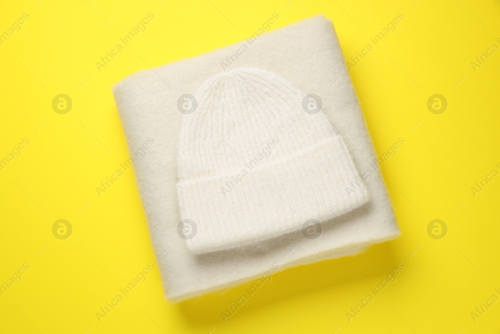 Photo of Warm woolen hat and scarf on yellow background, top view