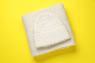 Photo of Warm woolen hat and scarf on yellow background, top view