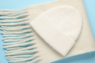 Photo of Warm woolen hat and scarf on light blue background, closeup