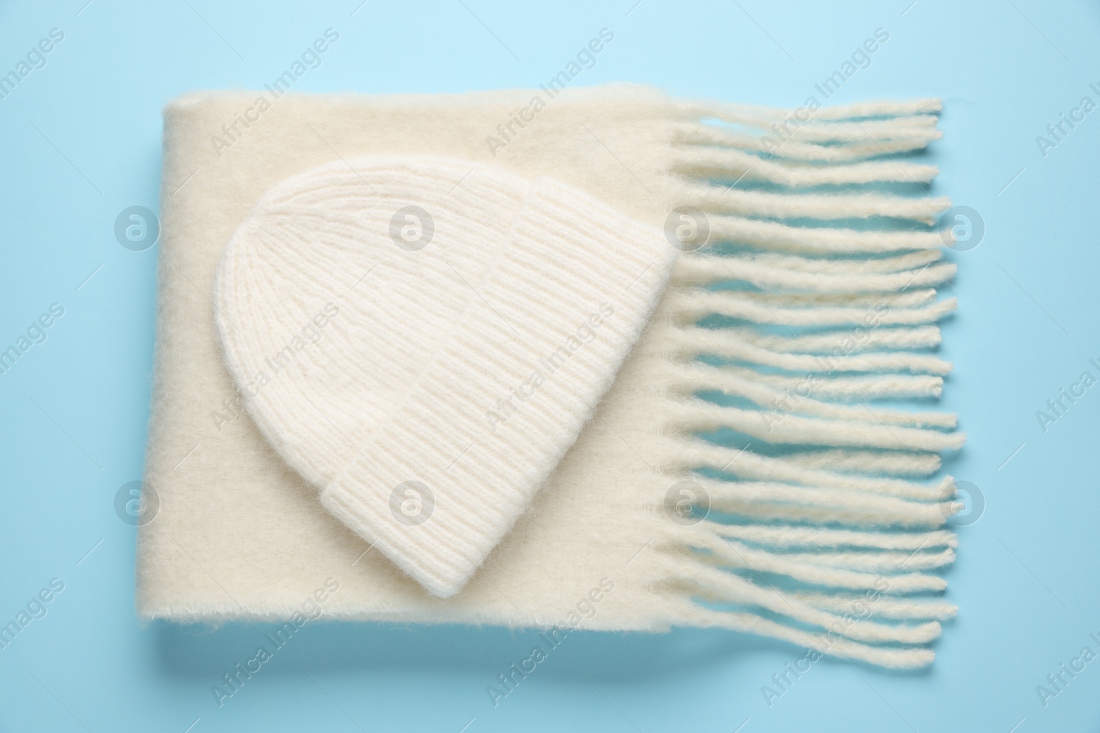 Photo of Warm woolen hat and scarf on light blue background, top view