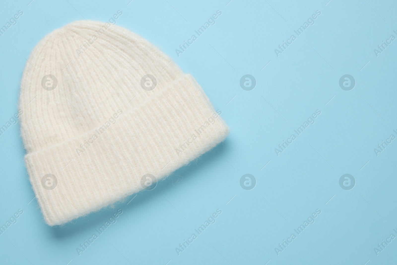 Photo of Warm woolen hat on light blue background, top view. Space for text