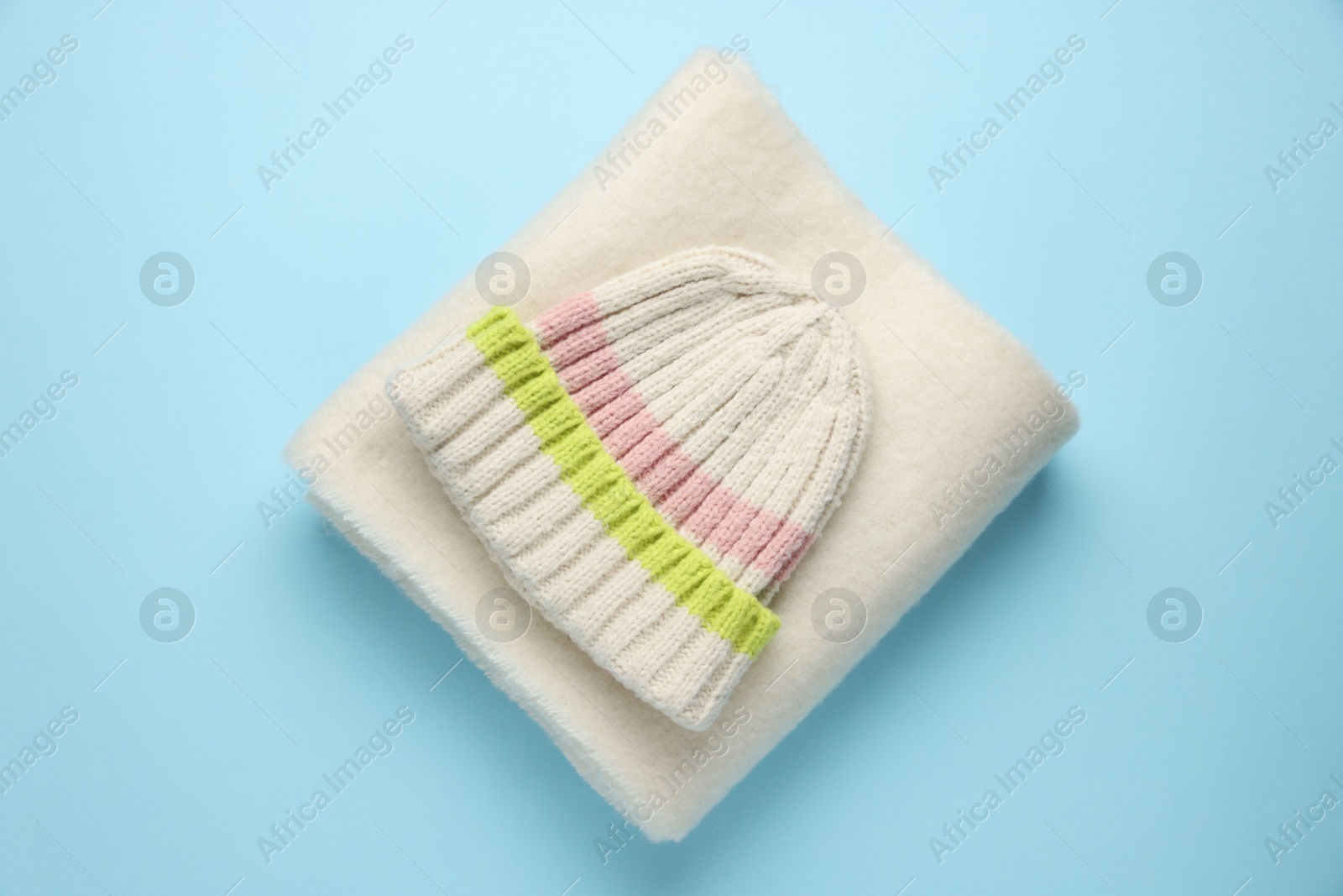 Photo of Warm woolen hat and scarf on light blue background, top view