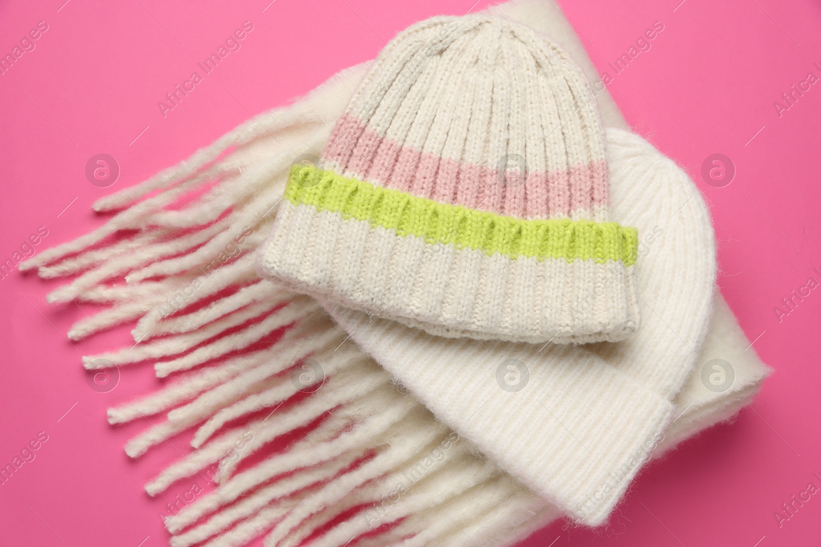 Photo of Warm woolen hats and scarf on pink background, closeup