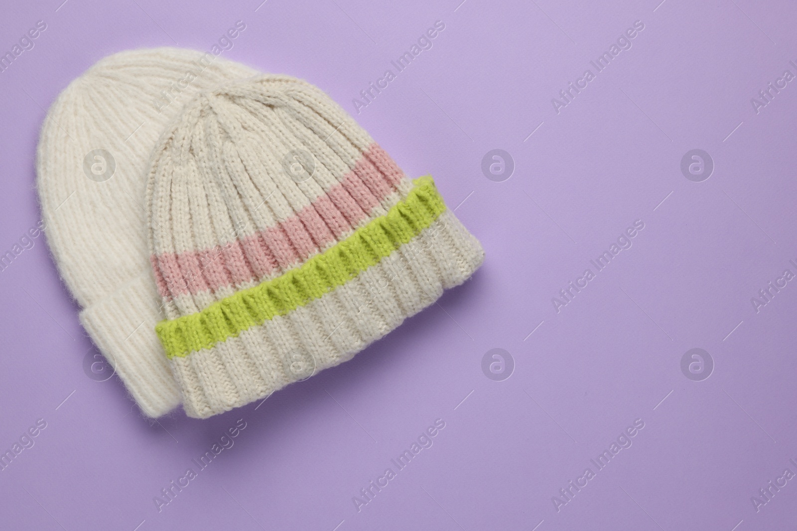 Photo of Warm woolen hats on lilac background, top view. Space for text