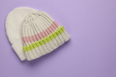 Photo of Warm woolen hats on lilac background, top view. Space for text