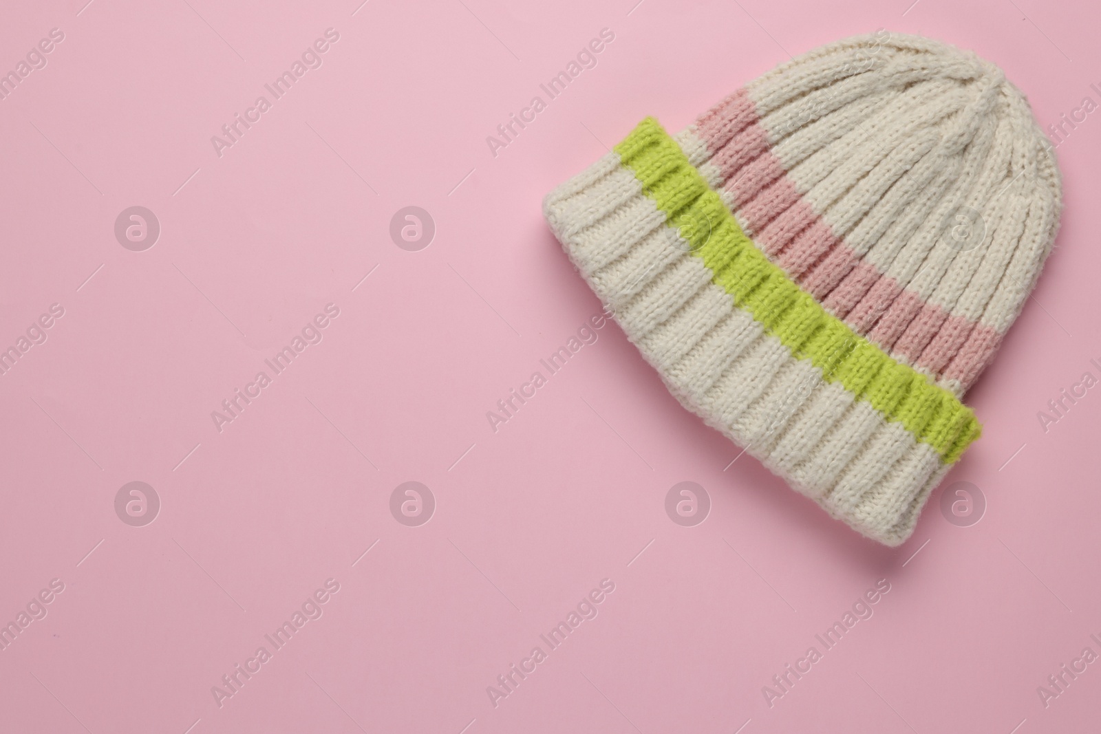 Photo of Warm woolen hat on light pink background, top view. Space for text