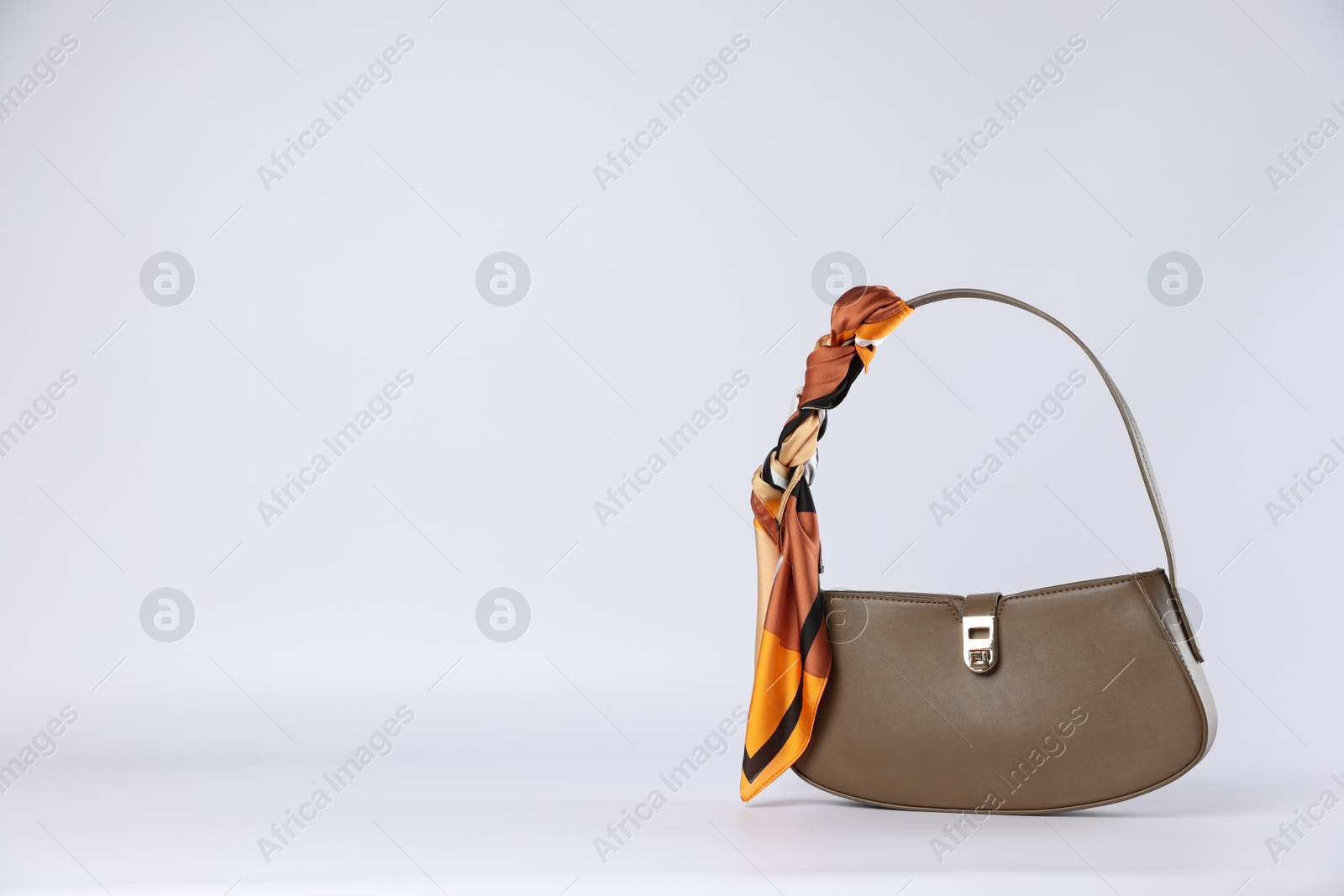 Photo of Elegant women baguette handbag with silk scarf on white background. Space for text