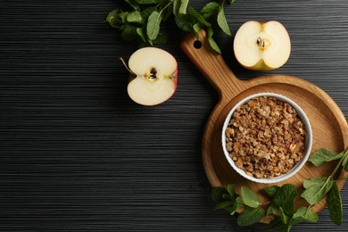 Photo of Delicious apple crisp in bowl, fresh fruits and mint on black textured table, flat lay. Space for text