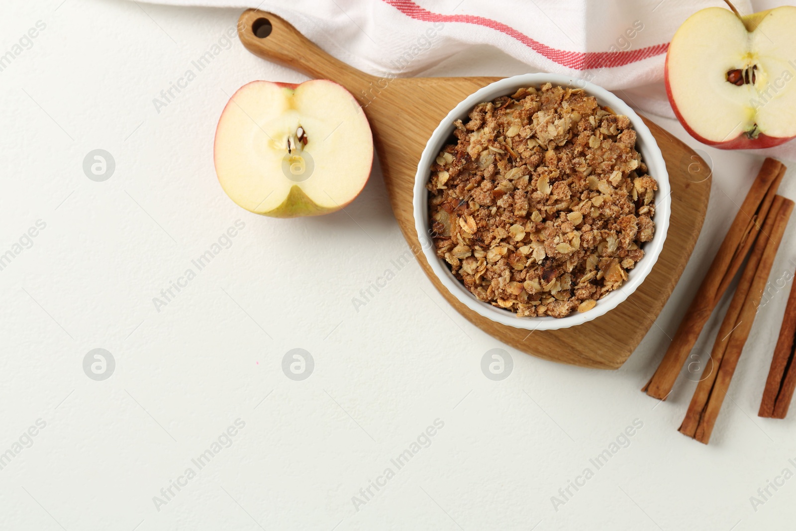 Photo of Delicious apple crisp in bowl, fresh fruits and cinnamon sticks on white table, flat lay. Space for text