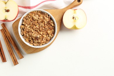 Photo of Delicious apple crisp in bowl, fresh fruits and cinnamon sticks on white table, flat lay. Space for text