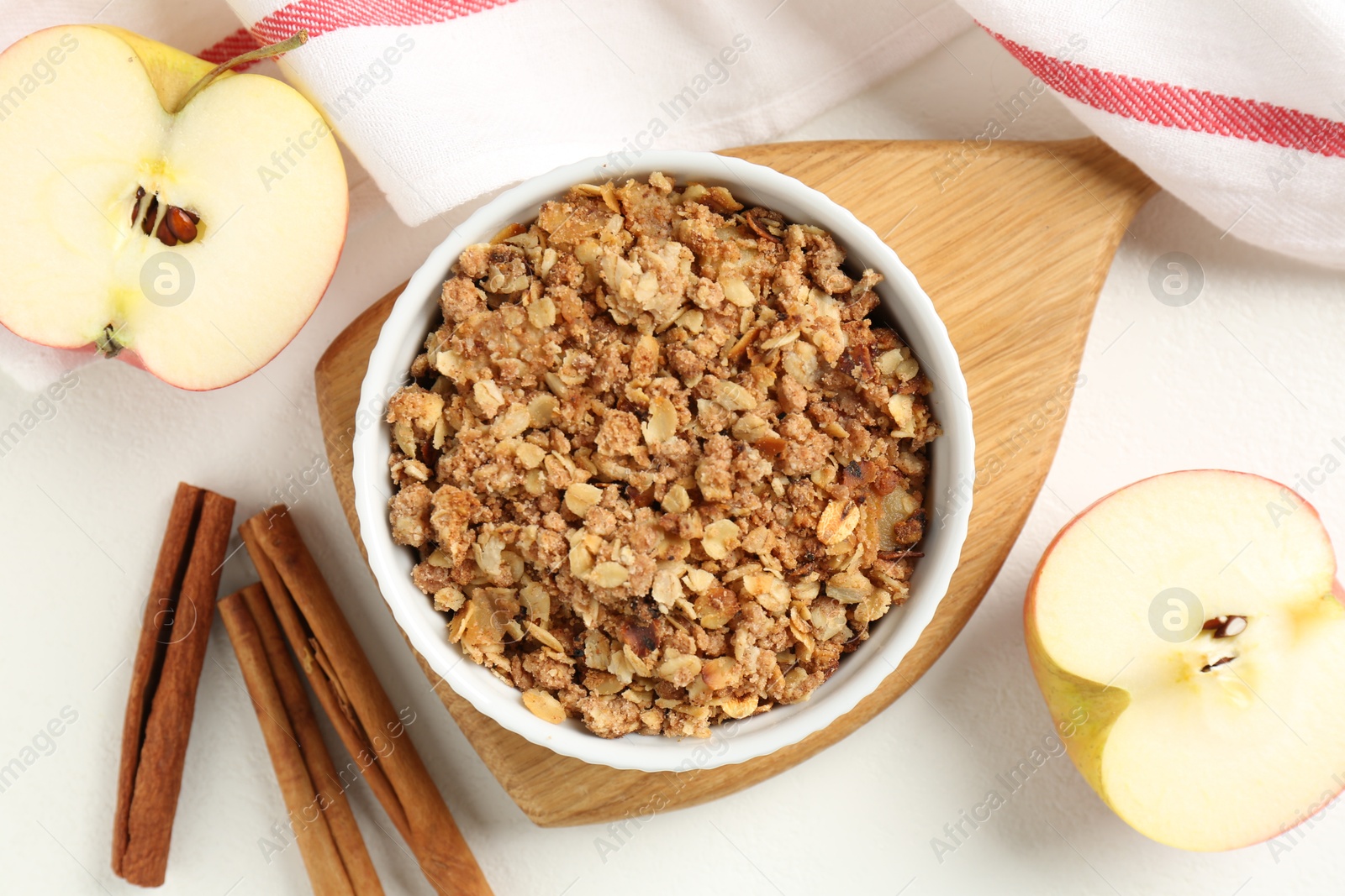 Photo of Delicious apple crisp in bowl, fresh fruits and cinnamon sticks on white table, flat lay