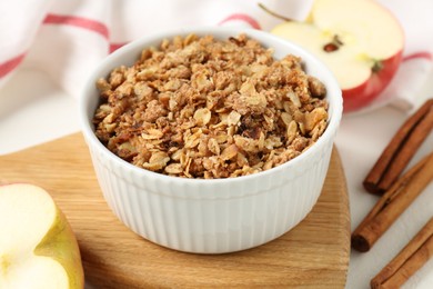 Photo of Delicious apple crisp in bowl, fresh fruits and cinnamon sticks on white table, closeup