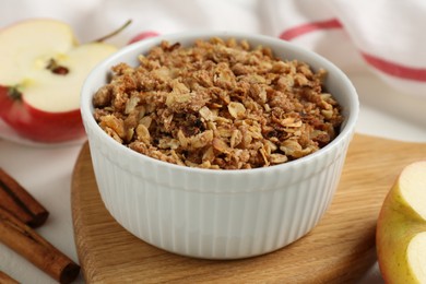 Photo of Delicious apple crisp in bowl, fresh fruits and cinnamon sticks on white table, closeup