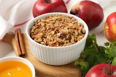 Photo of Delicious apple crisp in bowl, fresh fruits, mint, honey and cinnamon stick on table, closeup