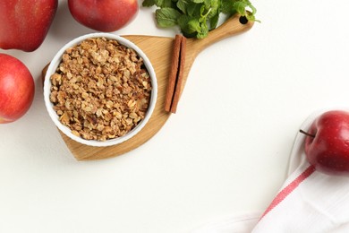 Photo of Delicious apple crisp in bowl, fresh fruits, mint and cinnamon stick on white table, flat lay. Space for text