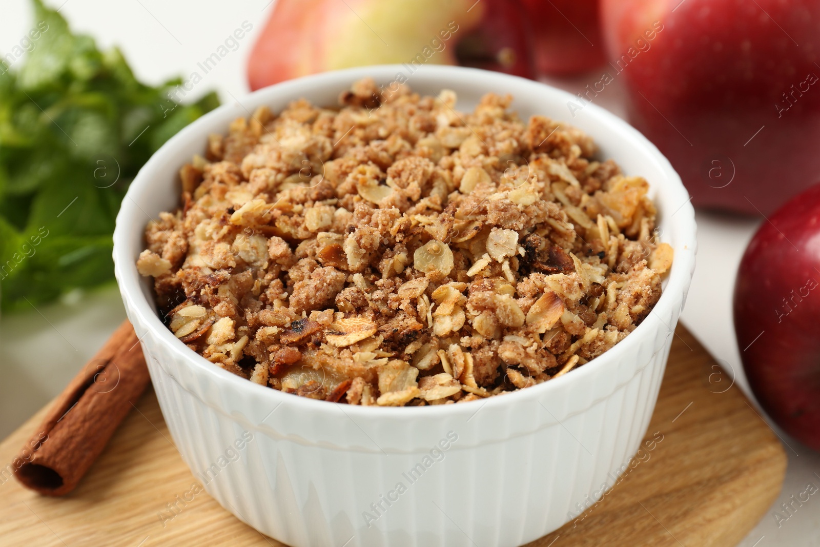 Photo of Delicious apple crisp in bowl, cinnamon, fresh fruits and mint on table, closeup