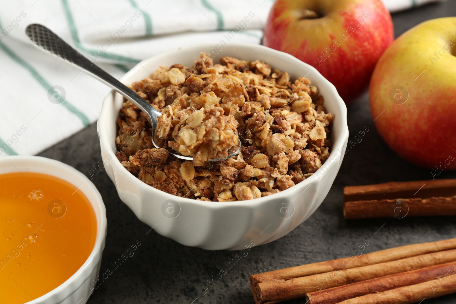 Photo of Delicious apple crisp in bowl, cinnamon sticks, fresh fruits and honey on grey table, closeup