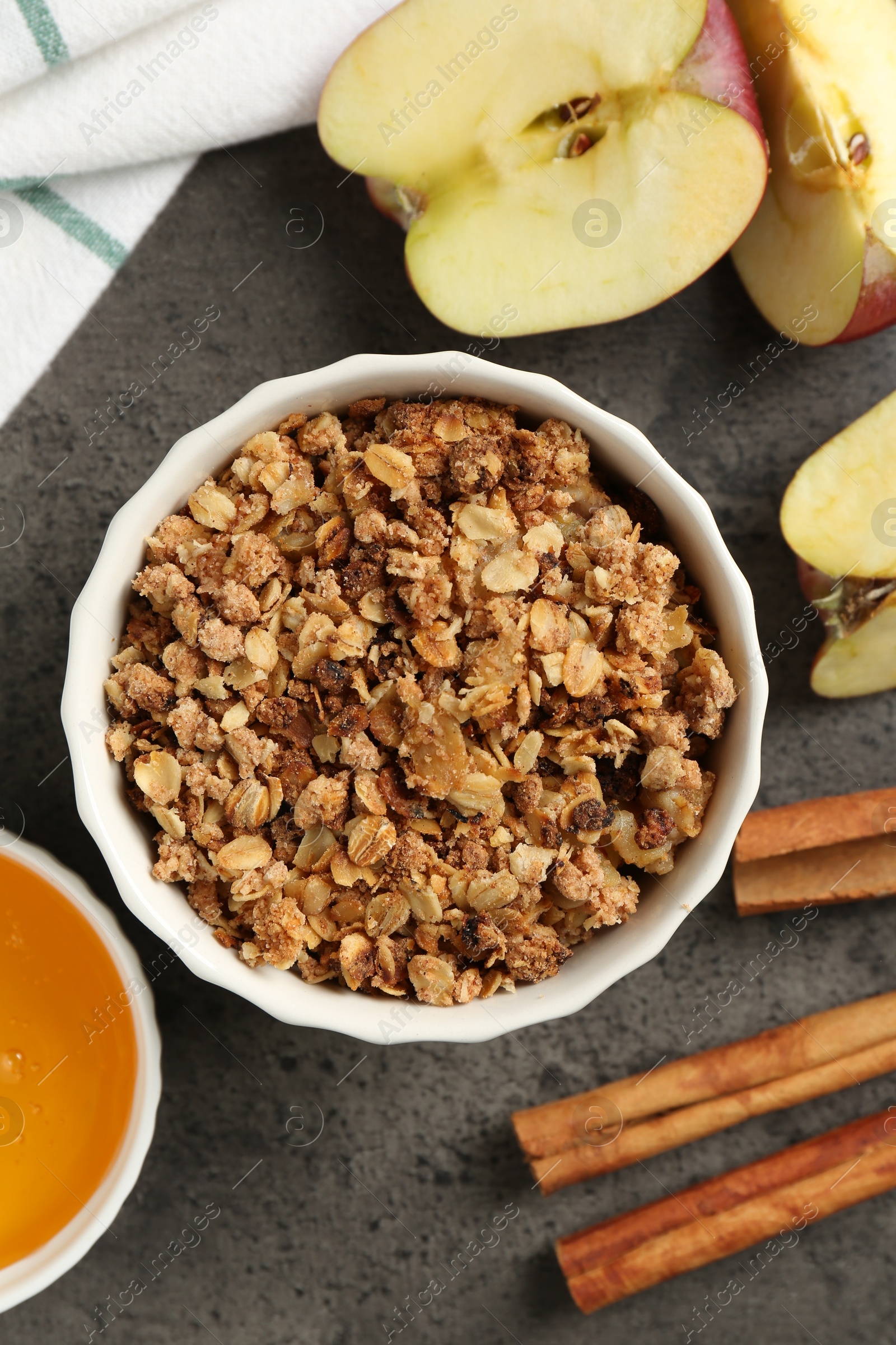 Photo of Delicious apple crisp in bowl, fresh fruits, cinnamon sticks and honey on grey table, flat lay