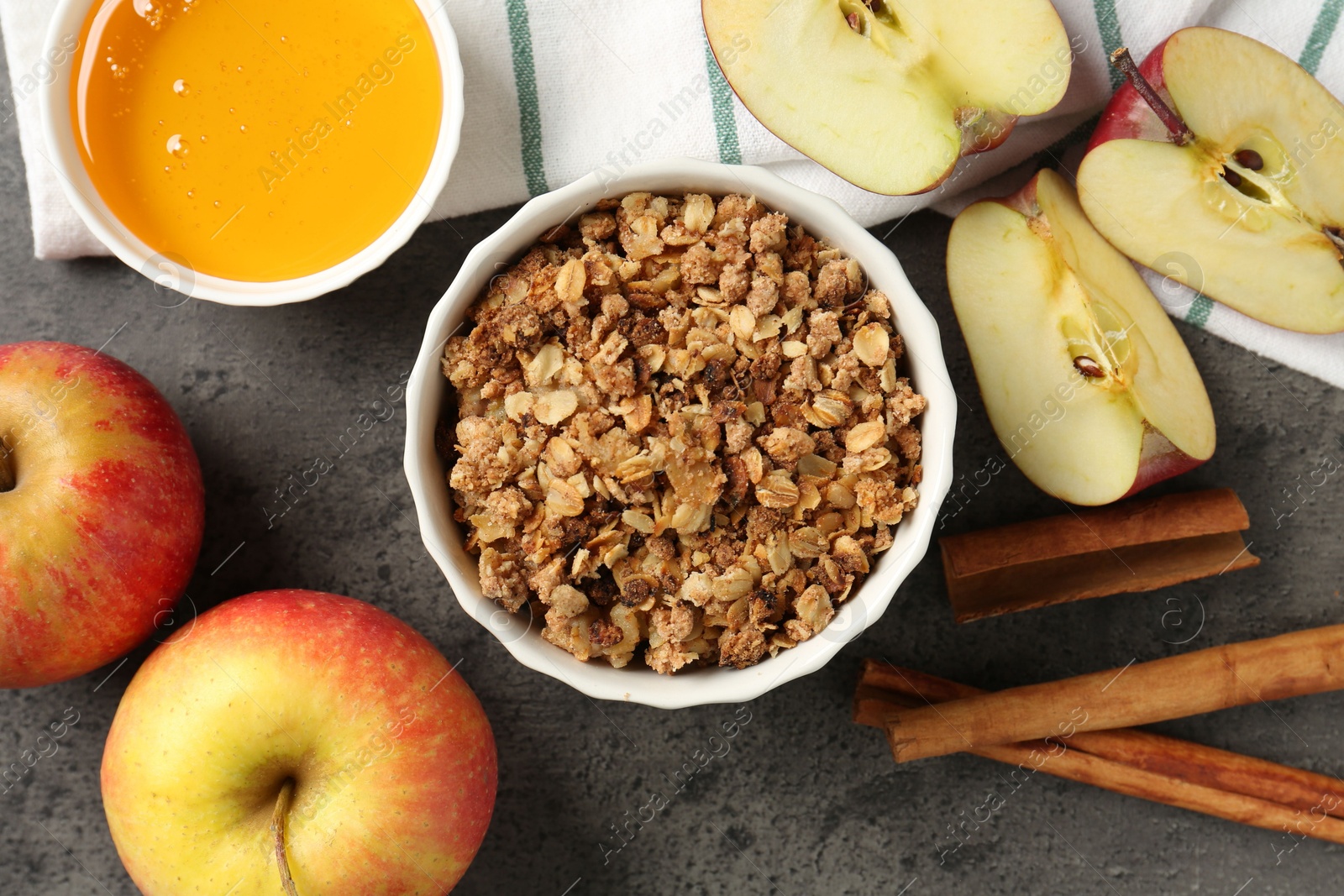 Photo of Delicious apple crisp in bowl, fresh fruits, cinnamon sticks and honey on grey table, flat lay