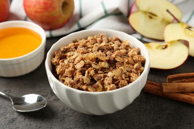 Photo of Delicious apple crisp in bowl, fresh fruits, cinnamon sticks and honey on grey table, closeup