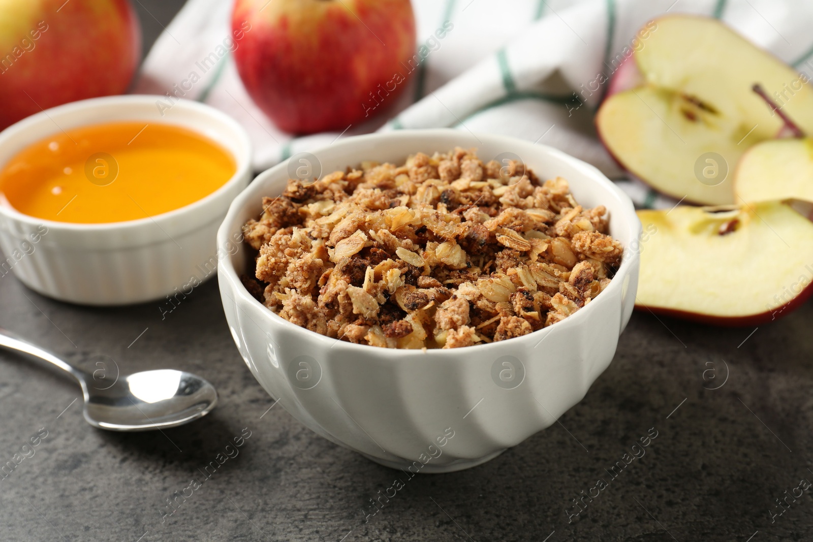 Photo of Delicious apple crisp in bowl, fresh fruits and honey on grey table, closeup