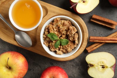 Photo of Delicious apple crisp in bowl, fresh fruits, cinnamon sticks, honey and mint on grey table, flat lay