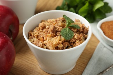 Photo of Delicious apple crisp in bowl, fresh fruits and mint on wooden table, closeup