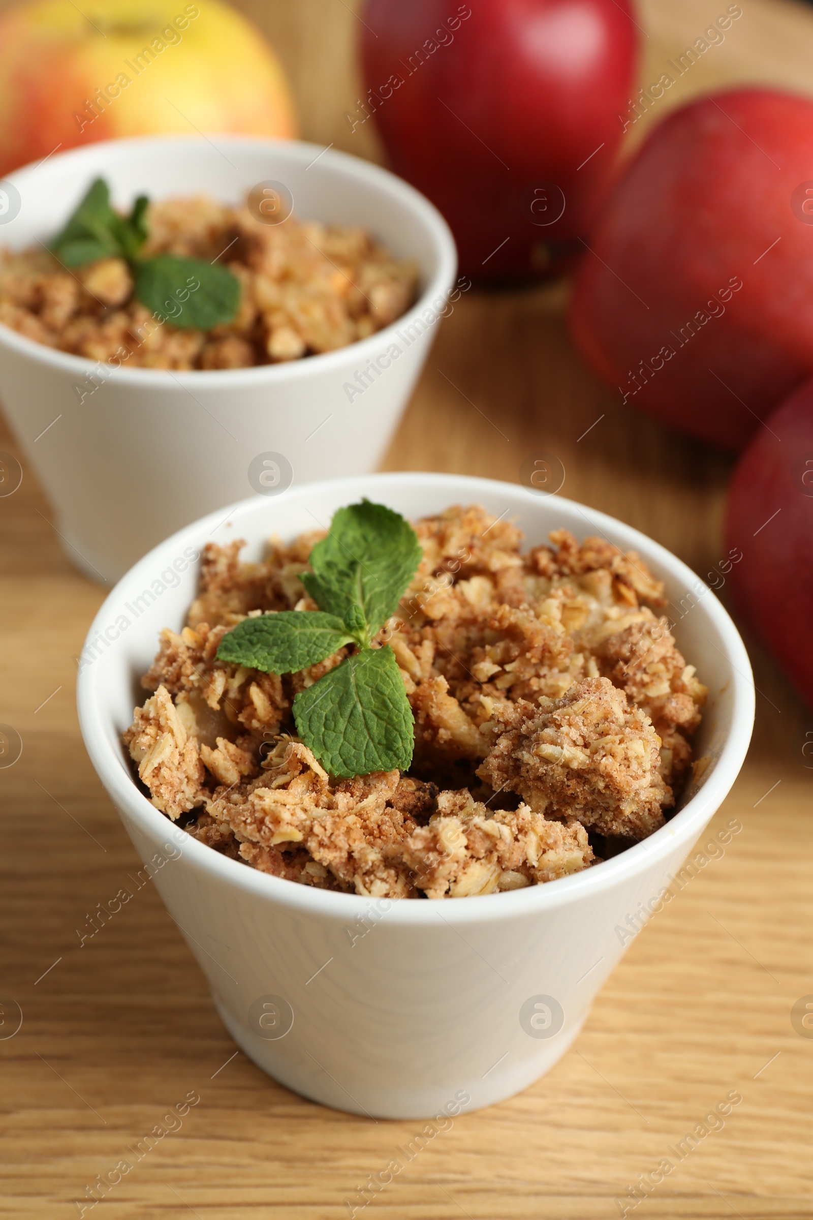 Photo of Delicious apple crisp with mint in bowls and fresh fruits on wooden table, closeup