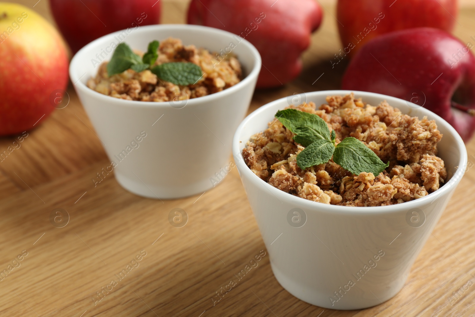 Photo of Delicious apple crisp with mint in bowls and fresh fruits on wooden table, closeup