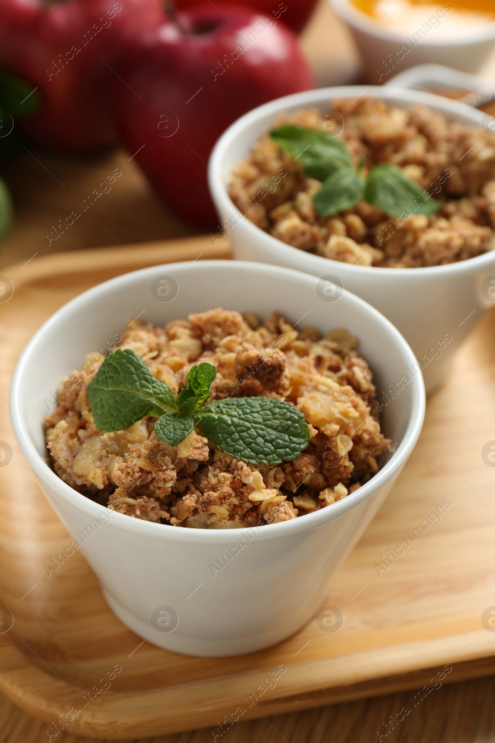 Photo of Delicious apple crisp with mint in bowls on table, closeup