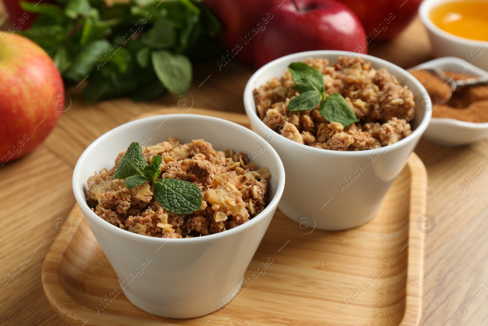 Photo of Delicious apple crisp with mint in bowls on wooden table, closeup