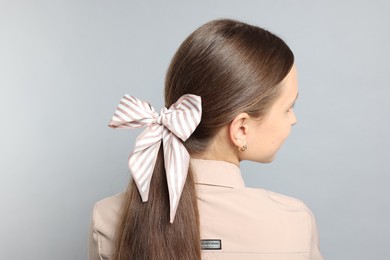 Photo of Teenage girl with stylish hair band on light grey background, back view