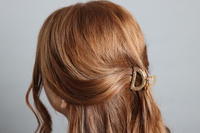 Teenage girl with stylish hair clip on light grey background, back view