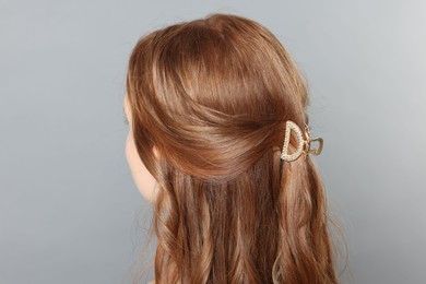 Teenage girl with stylish hair clip on light grey background, back view