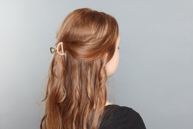 Teenage girl with stylish hair clip on light grey background, back view