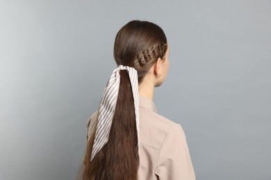 Photo of Teenage girl with stylish hair clips and bandana on light grey background, back view