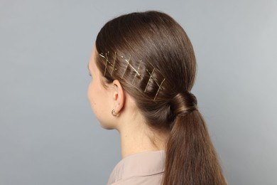 Photo of Teenage girl with stylish hair clips on light grey background, back view