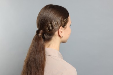 Teenage girl with stylish hair clips on light grey background, back view