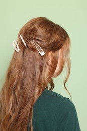 Photo of Teenage girl with stylish hair clips on light green background, back view