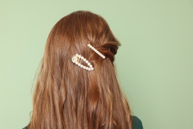 Teenage girl with stylish hair clips on light green background, back view