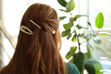 Photo of Teenage girl with stylish hair clips indoors, back view