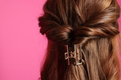 Teenage girl with stylish hair clip on pink background, back view