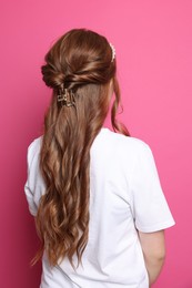 Photo of Teenage girl with stylish hair accessories on pink background, back view