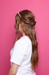 Photo of Teenage girl with stylish hair accessories on pink background, back view