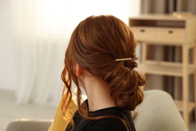 Teenage girl with stylish hair clip indoors, back view