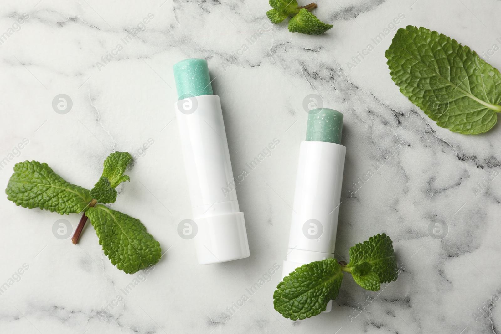 Photo of Natural lip balms and mint leaves on white marble background, flat lay