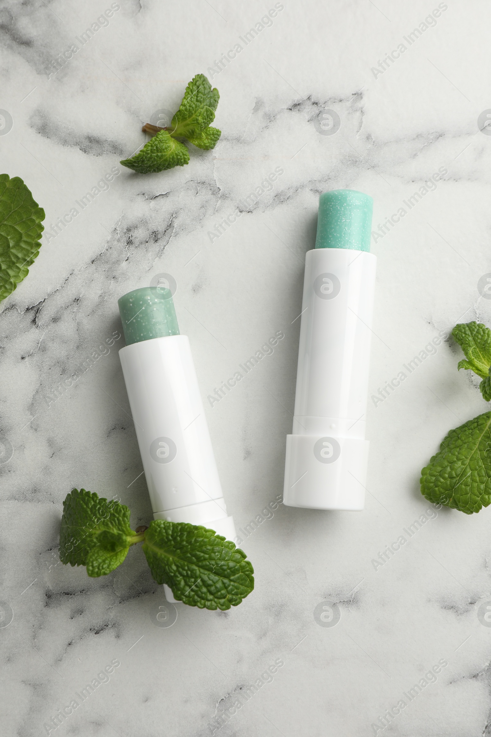 Photo of Natural lip balms and mint leaves on white marble background, flat lay