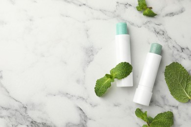 Photo of Natural lip balms and mint leaves on white marble background, flat lay. Space for text