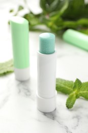 Photo of Natural lip balms and mint leaves on white marble background, closeup