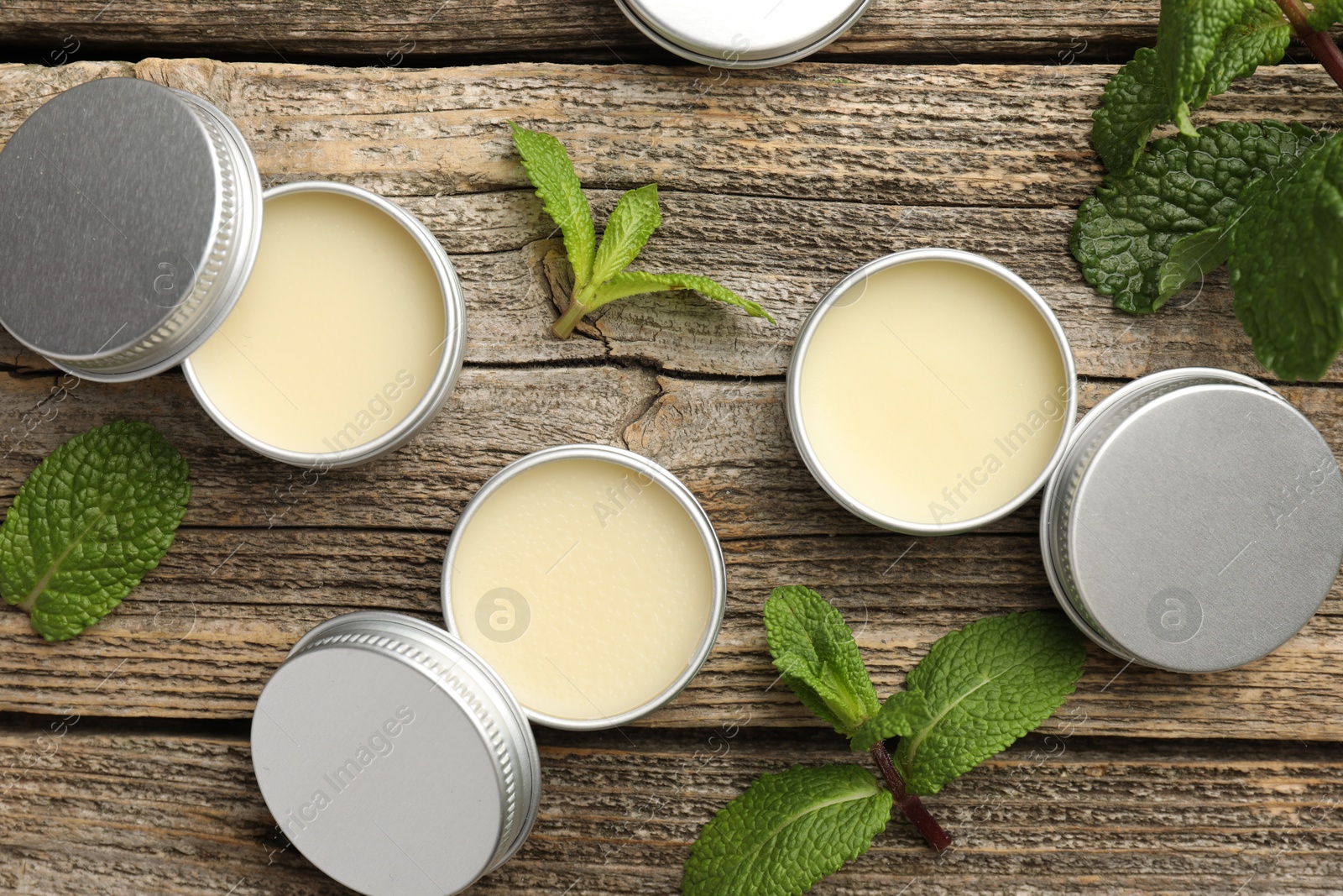 Photo of Natural lip balms and mint leaves on wooden background, flat lay